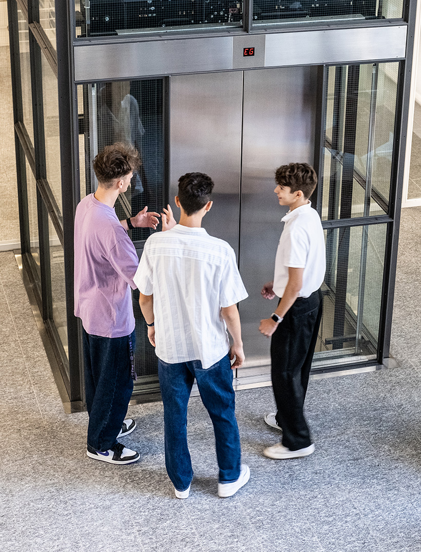 Trois apprentis discutent devant un ascenseur